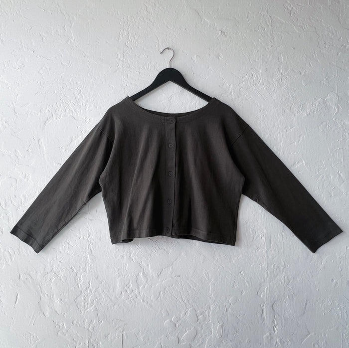 Dark green cropped cardigan on a hanger against a white wall