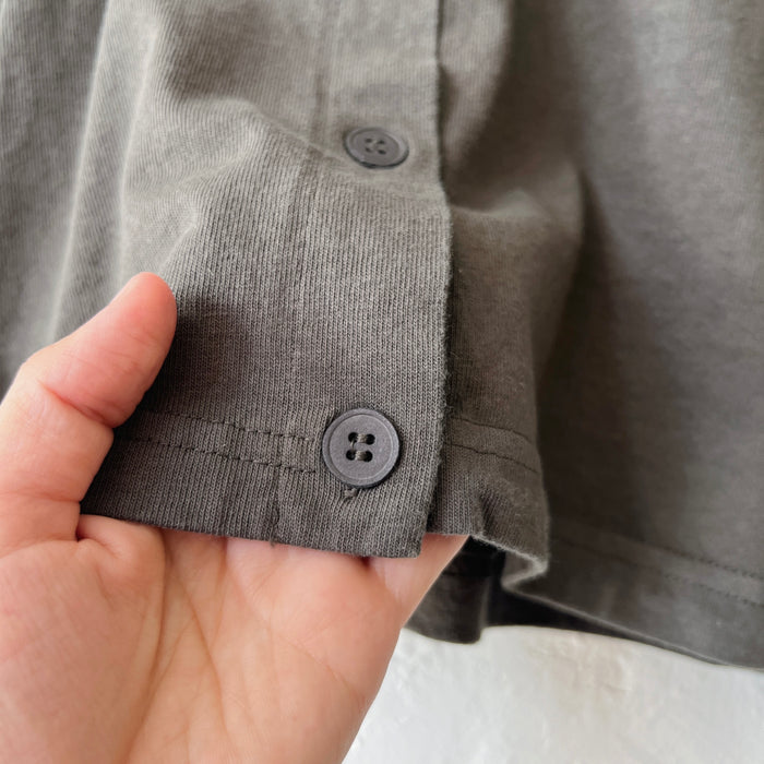Close-up of a hand holding a gray-green shirt hem with buttons.