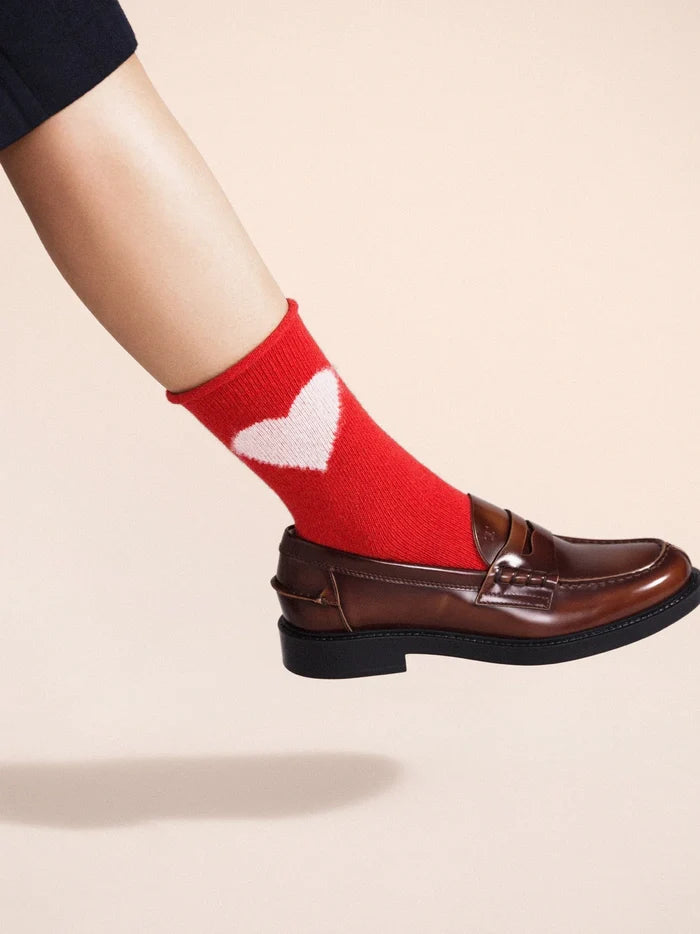 Love Cashmere Crew socks in Red — bold red cashmere crew with cream heart motif and roll cuff, worn with brown leather penny loafers on a cream background