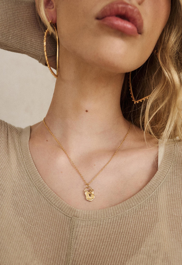 Close-up of gold Love Lock Charm Necklace on model, delicate chain with artisan lock pendant, styled with gold hoops