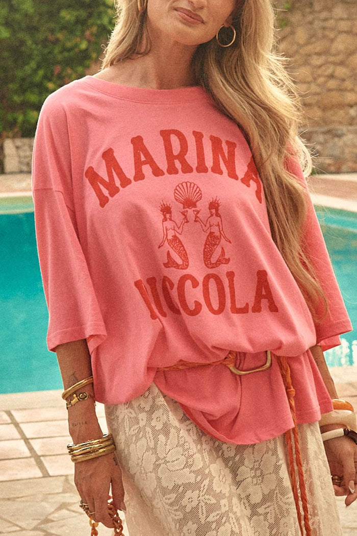 Front close-up of cosmos pink oversized tee with mermaid graphic print, styled with lace skirt and belt by pool