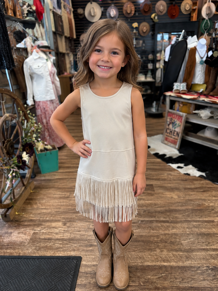 Young girl wearing a beige fringe dress and boots in a store setting.