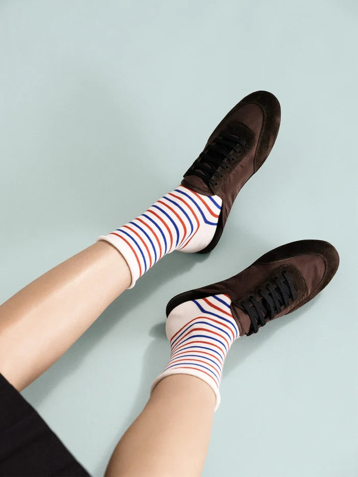 Nautical Stripe Crew socks in Bastille — cream crew with alternating red and blue horizontal stripes and rolled cuff, worn with dark brown lace-up sneakers on a light blue background