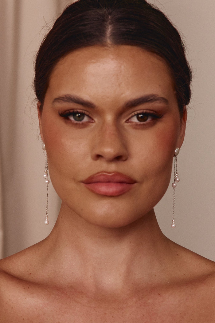 Close-up of a woman wearing pearl earrings with a neutral background