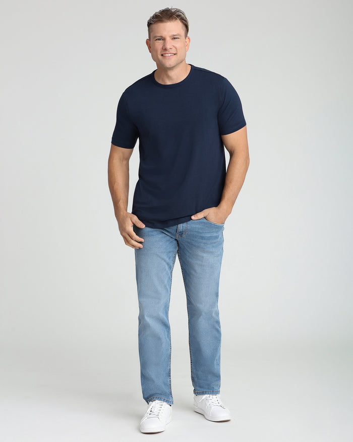 Man wearing navy crew neck short-sleeve t-shirt with light blue jeans and white sneakers.