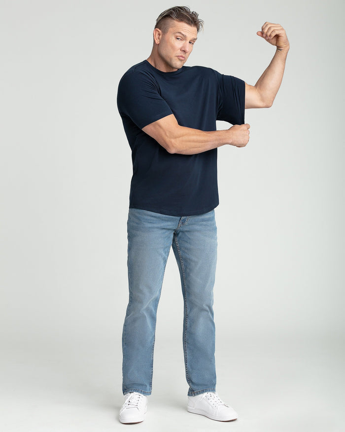 Man wearing navy crew neck t-shirt with light blue jeans and white sneakers, demonstrating fit.