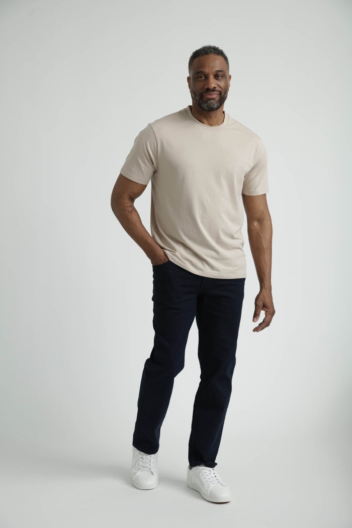 Tan crew neck t-shirt with short sleeves on a model wearing dark pants and white sneakers.