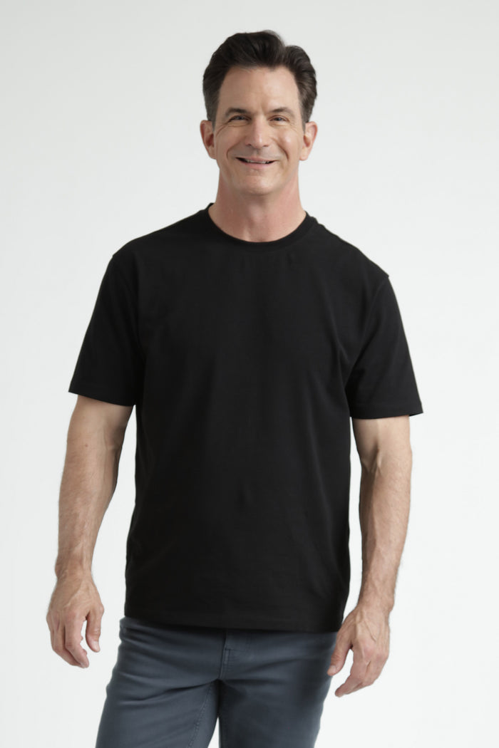 Man wearing black crew neck t-shirt with short sleeves and gray pants against white background.