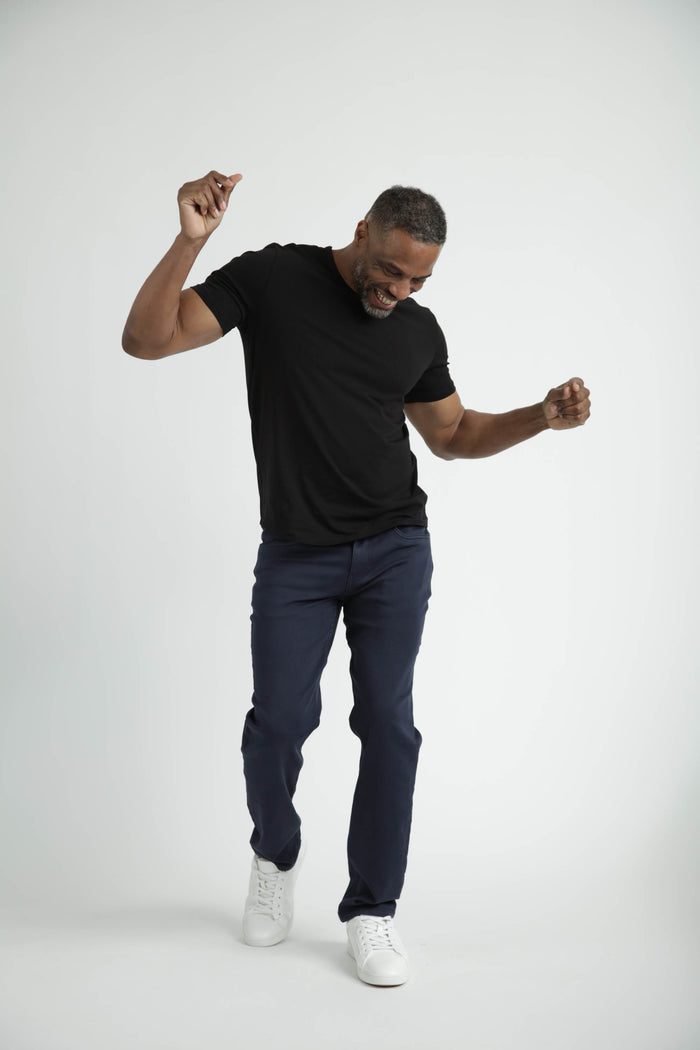 Man wearing black crew neck t-shirt with dark navy pants and white sneakers.
