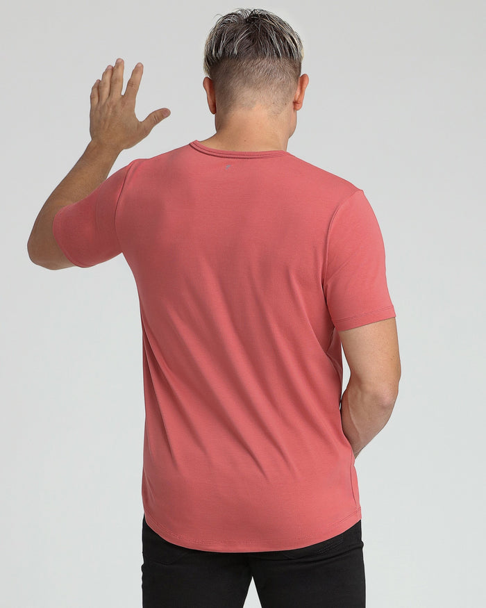 Man wearing coral crew neck t-shirt with short sleeves and black pants, shown from back view.