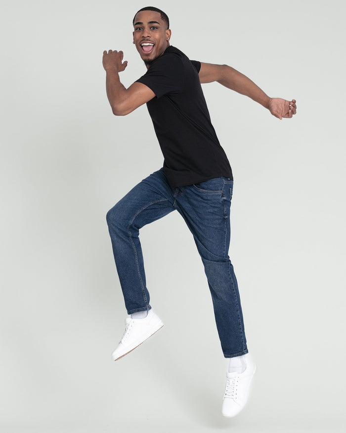 Man wearing black crew neck t-shirt with blue jeans and white sneakers.