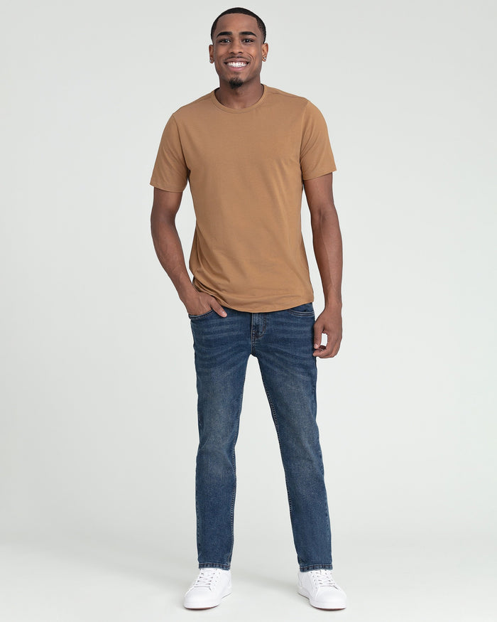 Man wearing tobacco crew neck t-shirt with blue jeans and white sneakers.