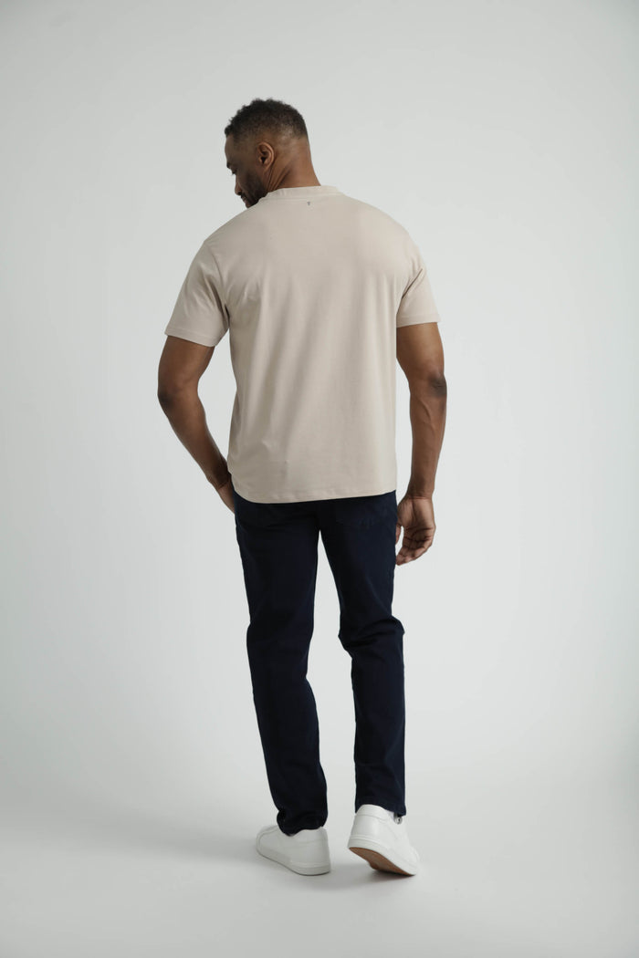 Man wearing tan crew neck t-shirt with short sleeves and dark pants, shown from back view.