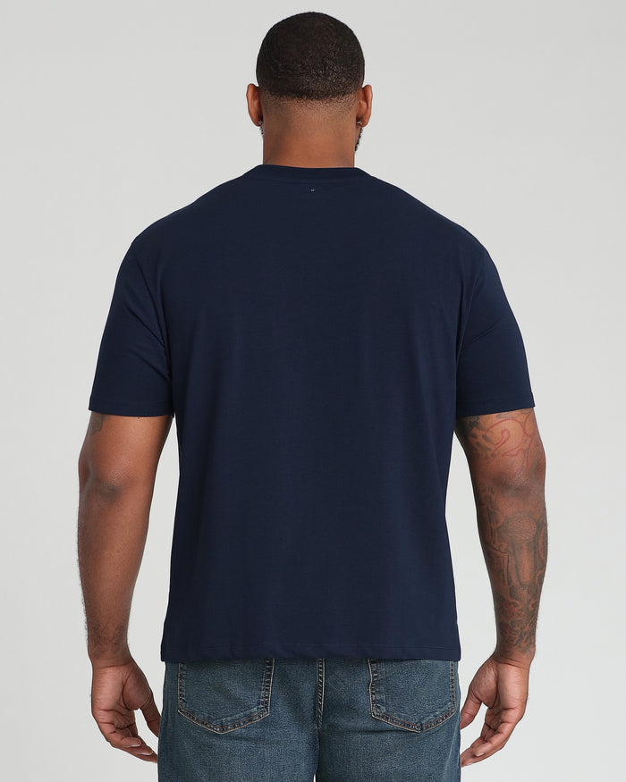 Man wearing navy crew neck t-shirt, shown from back, paired with blue jeans.