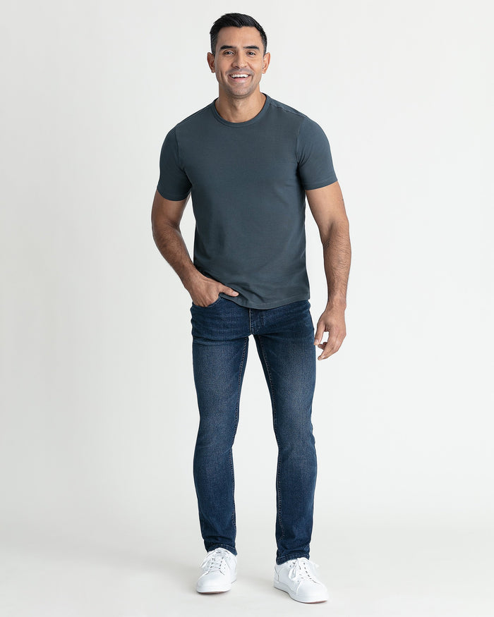 Man wearing steel gray crew neck t-shirt with dark jeans and white sneakers.