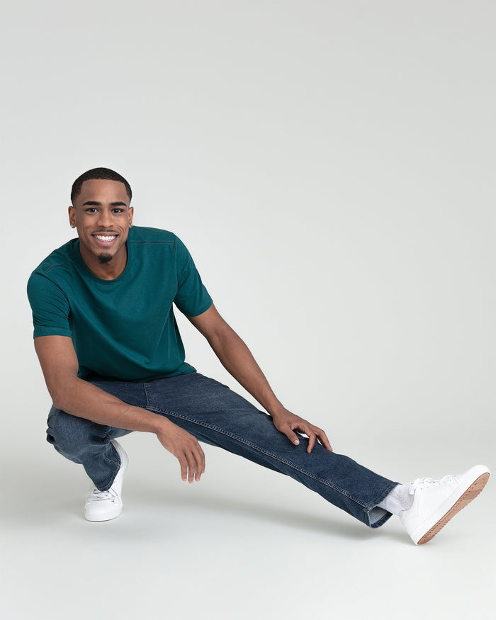 Man wearing teal crew neck short-sleeve t-shirt with dark jeans and white sneakers.