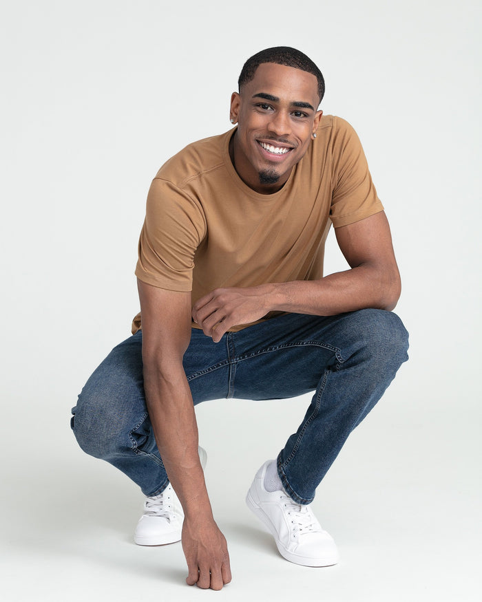 Man wearing tobacco-colored crew neck t-shirt with dark jeans and white sneakers.
