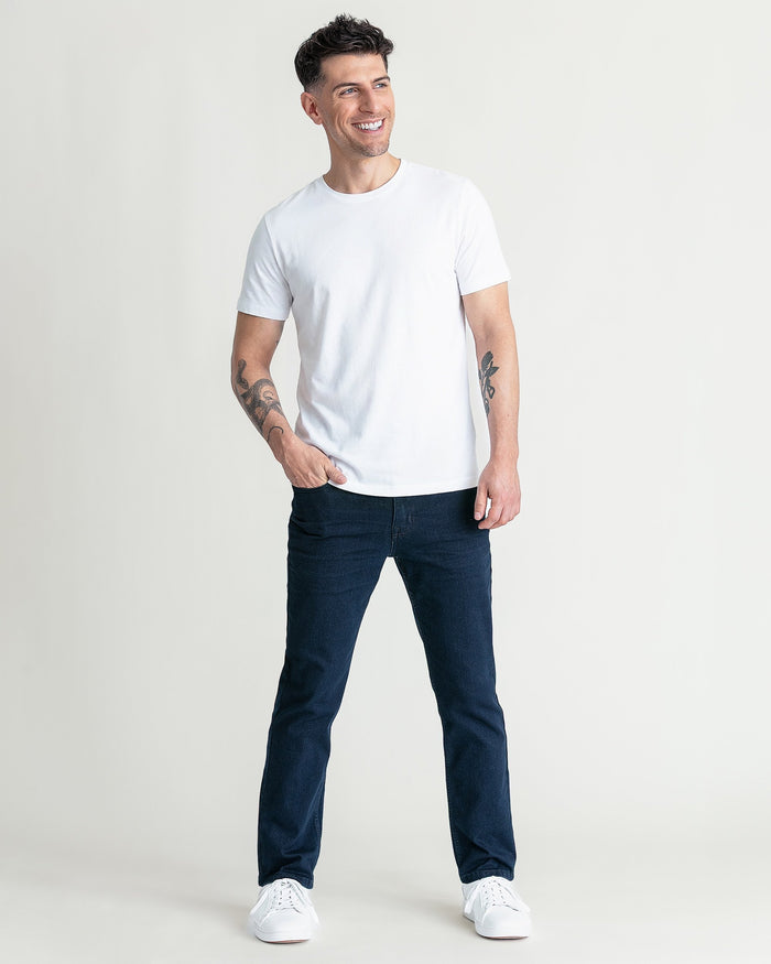 Man wearing white crew neck short-sleeve t-shirt with dark jeans and white sneakers.