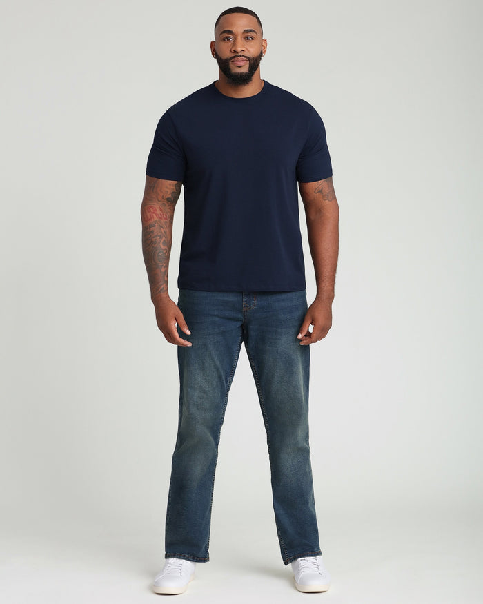 Navy crew neck t-shirt with short sleeves on a man wearing jeans and white sneakers.