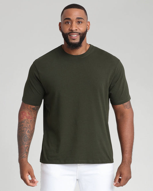 Man wearing olive crew neck t-shirt with white shorts against neutral background.