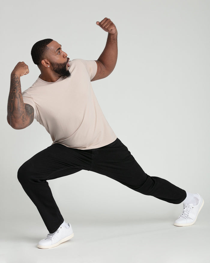Tan crew neck t-shirt with short sleeves on model in athletic pose with black pants and white sneakers.