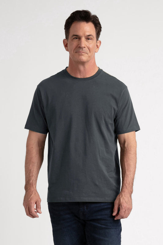 Man wearing steel gray crew neck t-shirt with short sleeves and dark jeans against white background.
