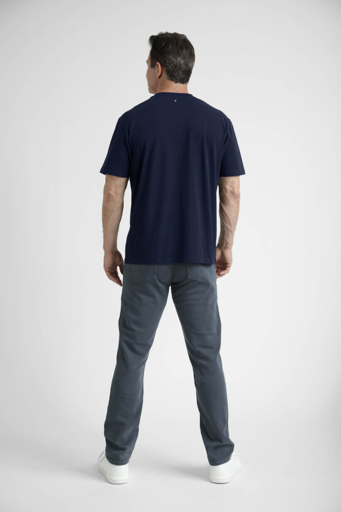 Man wearing navy crew neck t-shirt with short sleeves and gray pants, shown from back view.