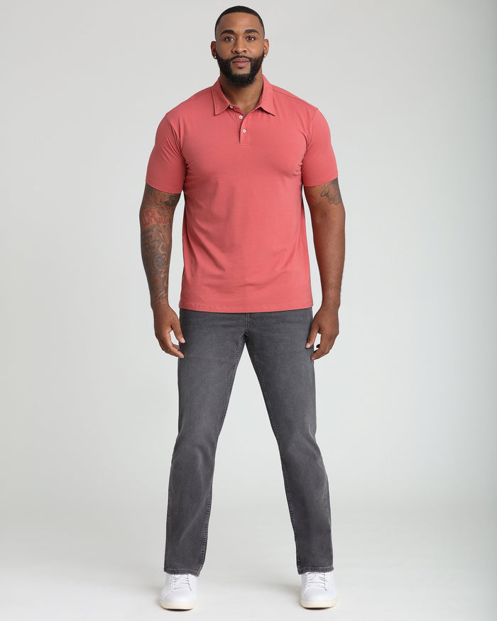 Man wearing nantucket red short-sleeve polo shirt with white buttons and gray jeans.