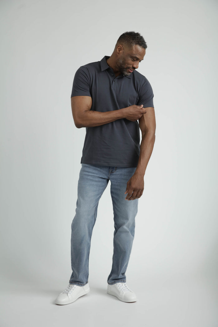 Man wearing dark grey short-sleeve polo shirt with collar, paired with light blue jeans and white sneakers.