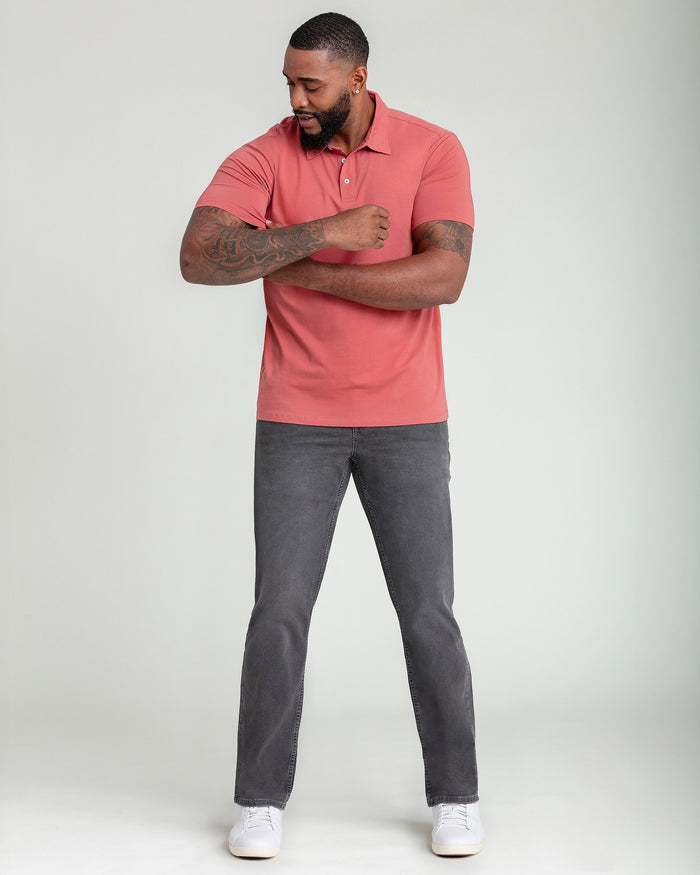 Man wearing nantucket red short-sleeve polo shirt with button placket and gray jeans.