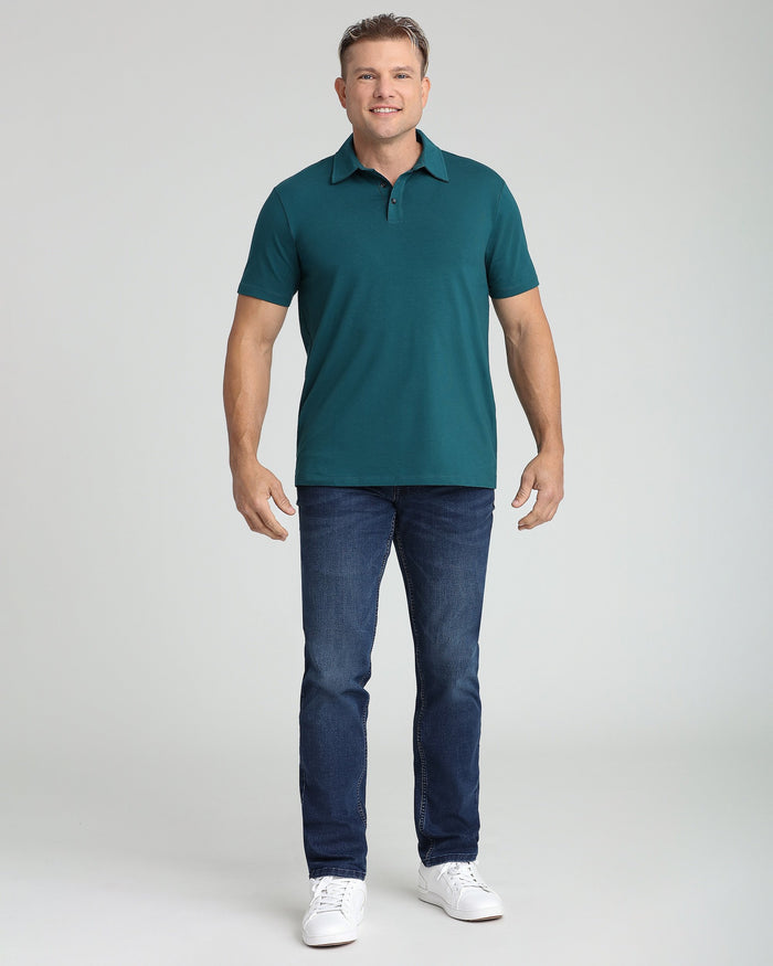 Man wearing teal short-sleeve polo shirt with collar and buttons, paired with dark jeans and white sneakers.