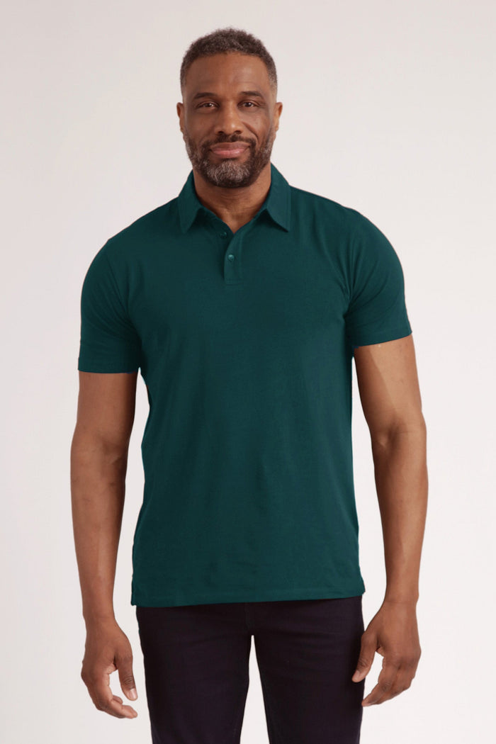 Man wearing dark teal short-sleeve polo shirt with button placket and black pants against neutral background.