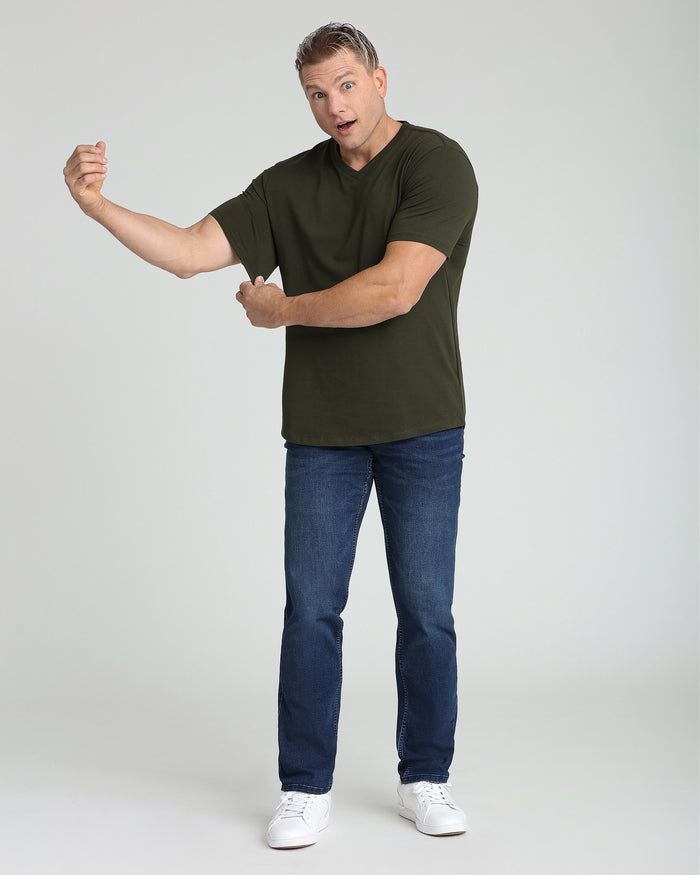 Man wearing olive v-neck short-sleeve t-shirt with blue jeans and white sneakers.