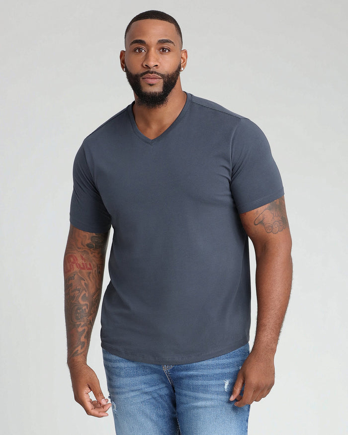 Man wearing dark gray v-neck t-shirt and blue jeans against white background.