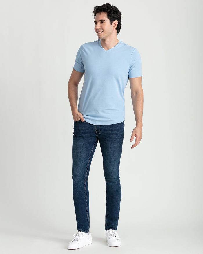 Man wearing light blue v-neck t-shirt and dark jeans with white sneakers.