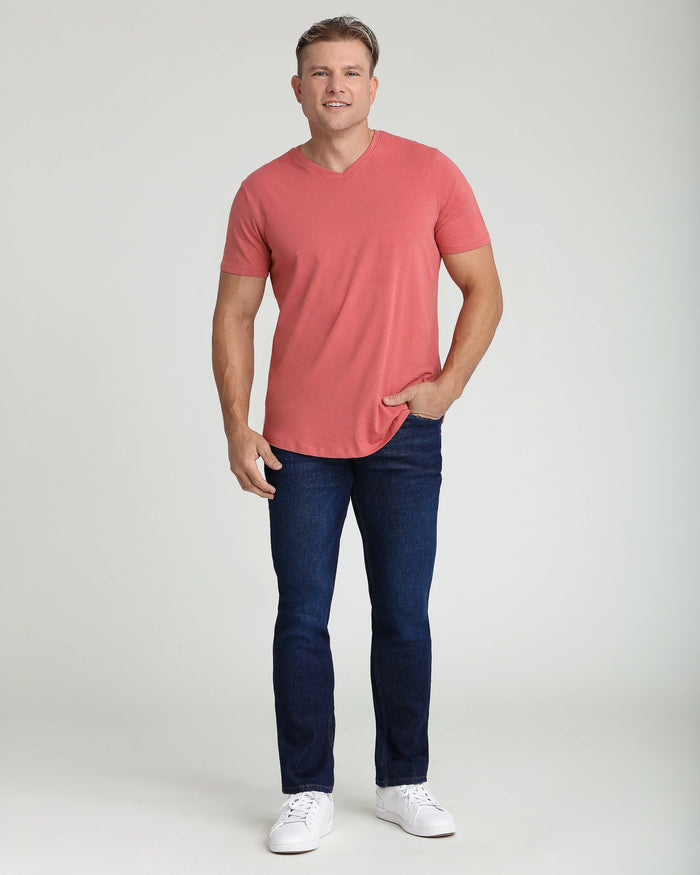 Man wearing coral V-neck t-shirt with short sleeves and dark blue jeans.