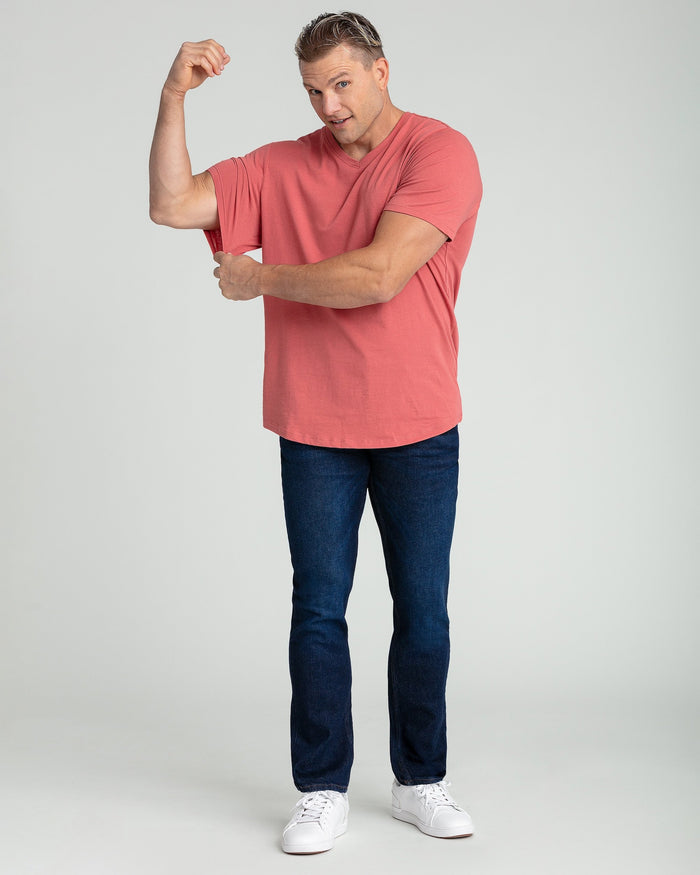Man wearing salmon-colored V-neck t-shirt with dark jeans and white sneakers.