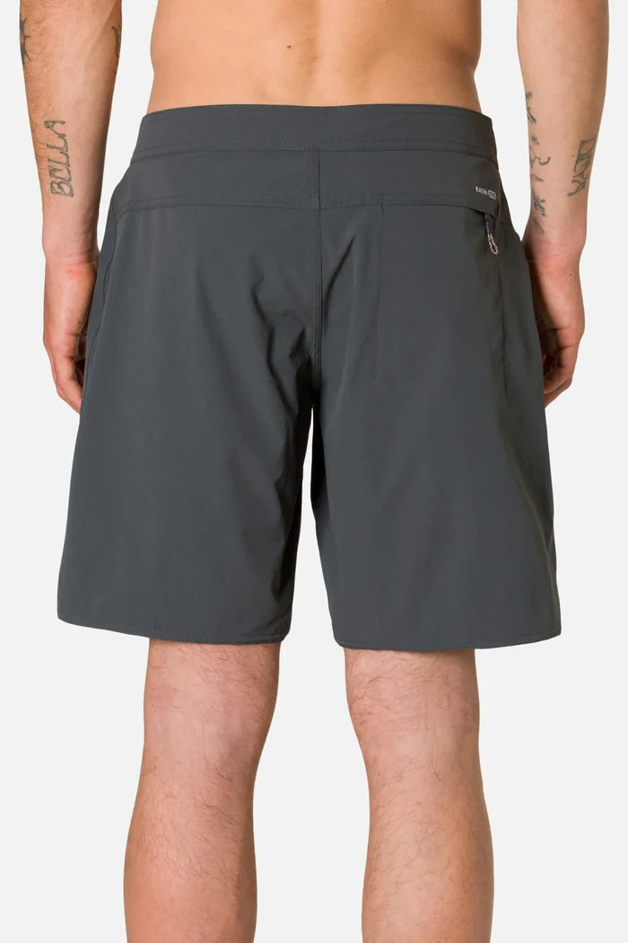 Rear view of a tattooed man wearing the Katin OTG Crest Surf Trunk in Black Wash, showing the back zip pocket with a gold zipper pull and the Katin wordmark printed on the waistband