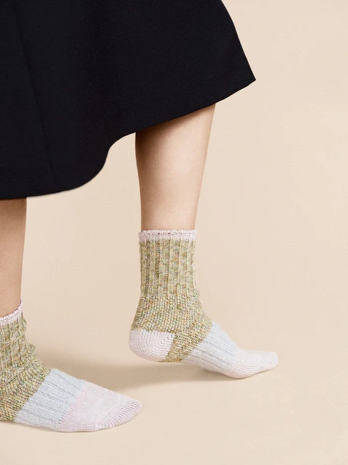 Pixie Dapple Crew socks in Pastel — sage and gold slub cotton crew with white heel and pink rolled cuff, worn barefoot on tiptoe under a black midi skirt on a cream background
