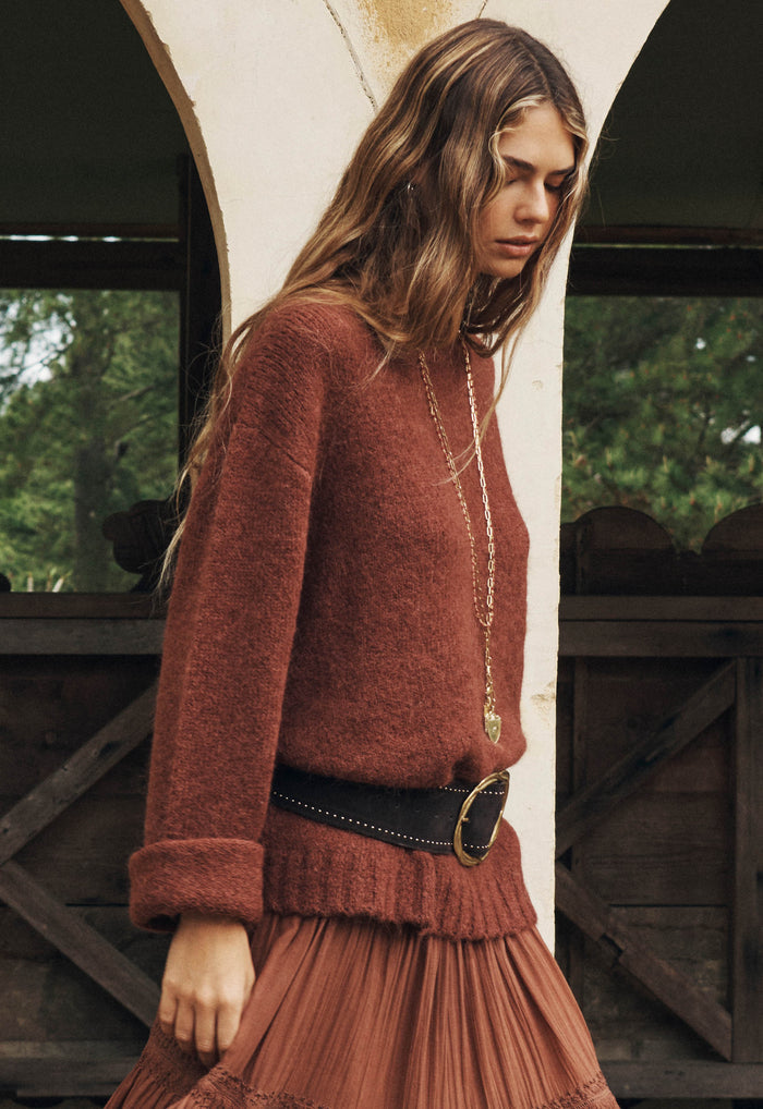 Model wearing cocoa alpaca-wool sweater, side angle showing ribbed cuffs and hem, styled with belt and pleated skirt