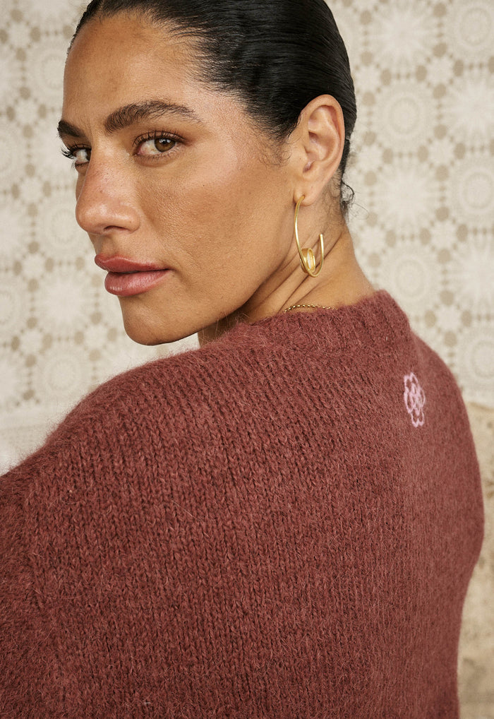 Back view close-up of a model in cocoa alpaca-wool knit sweater showing custom Spell embroidery on shoulder