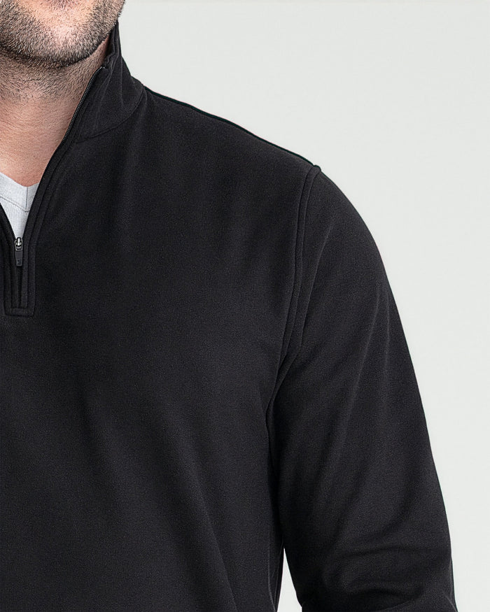 Black quarter zip pullover worn by man, showing chest and shoulder detail with white undershirt visible at neckline.