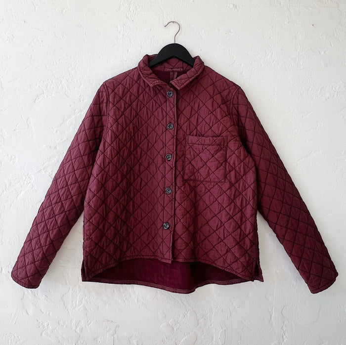 Quilted maroon jacket with a diamond pattern on a hanger against a white wall