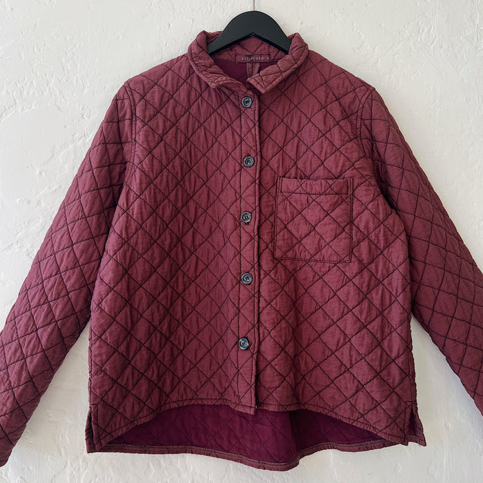 Quilted maroon jacket with a diamond pattern on a hanger against a white wall