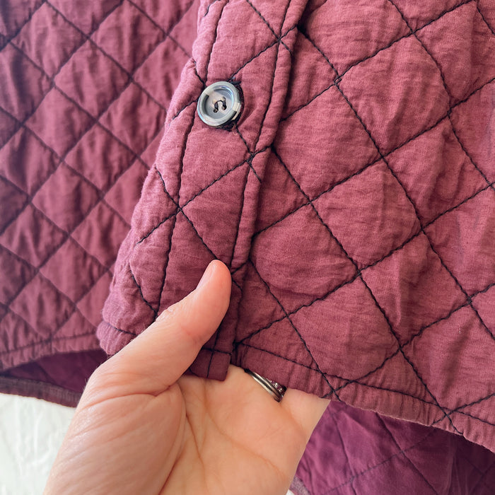 Close-up of a hand holding a quilted maroon fabric with a button.