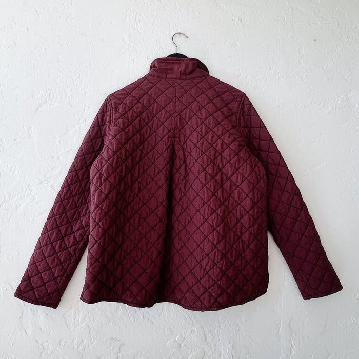 Quilted jacket on a hanger against a white wall, viewed from the back