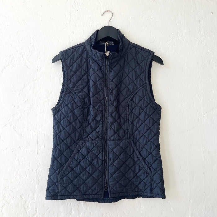 Navy quilted vest on a hanger against a white wall