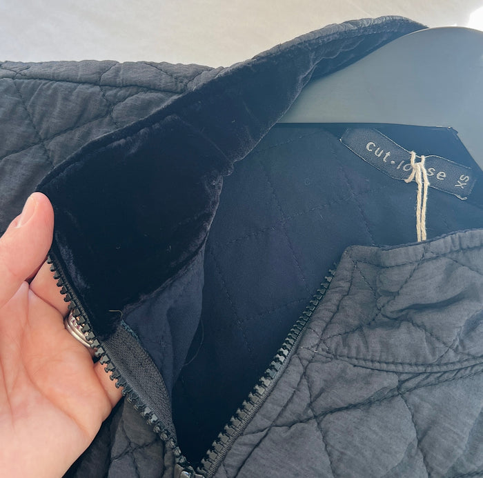 Hand holding the collar of a navy quilted jacket with a brand label 'cut loose'