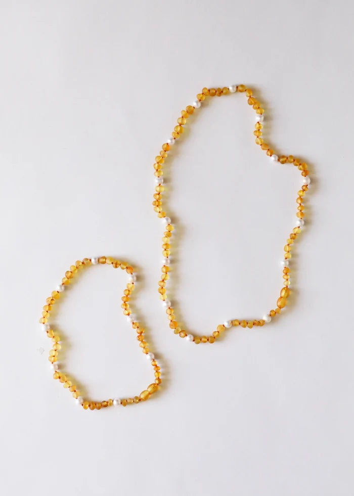 A pair of hand-knotted beaded necklaces alternating  honey amber beads in golden yellow with pearl beads, with a screw clasp, laid flat on a white background, shown in two lengths: 13" and 16"