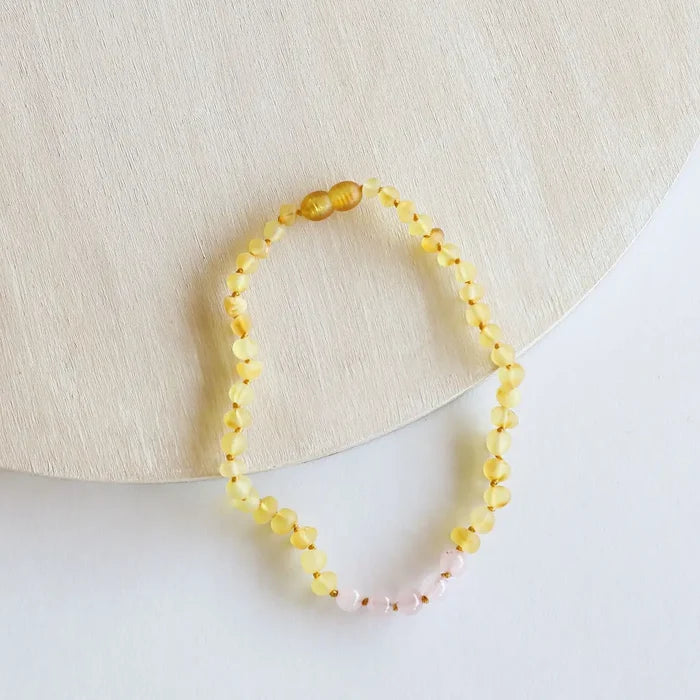 CanyonLeaf raw honey Baltic amber and rose quartz beaded necklace with hand-knotted cord and screw clasp, laid flat on a light wood and white background